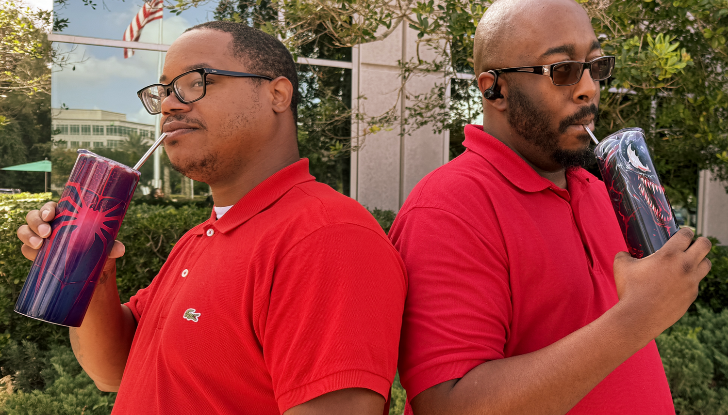 Two men in red shirts holding colorful drinks outdoors.