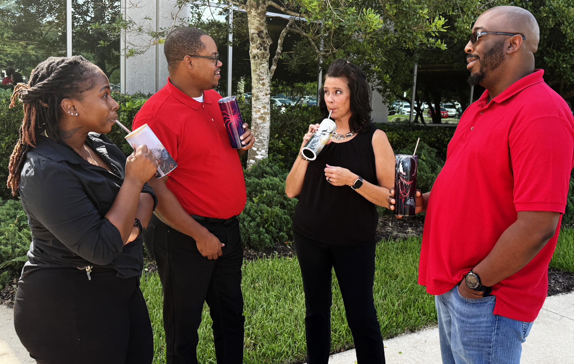 Four people engaged in a conversation outdoors with trees and buildings in the background